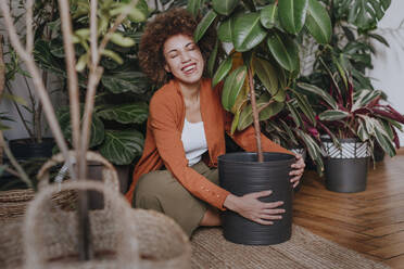 Glückliche Frau sitzt mit Pflanzen auf einem Teppich - YTF01835