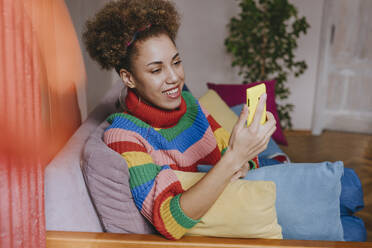 Smiling woman using smart phone on sofa - YTF01847