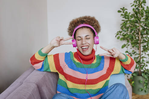 Happy woman listening to music and showing peace sign gesture - YTF01864