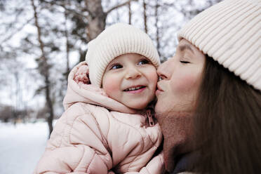 Young mother kissing daughter at winter park - MBLF00261