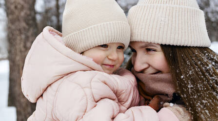 Lächelnde Mutter und Tochter mit Strickmützen im Winterpark - MBLF00262
