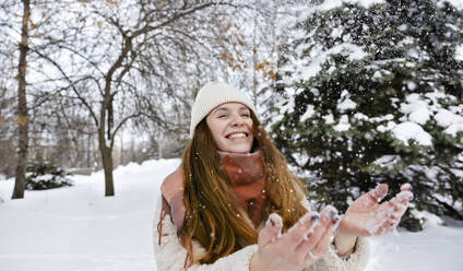Fröhliche Frau spielt mit Schnee im Winterpark - MBLF00263