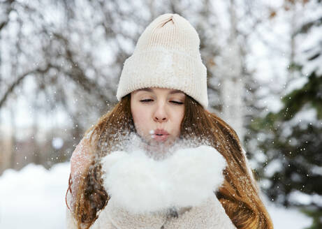 Verspielte Frau bläst auf Schnee im Winterpark - MBLF00264