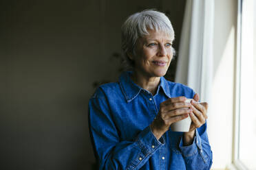 Lächelnde reife Frau hält Kaffeetasse zu Hause - EBSF04379