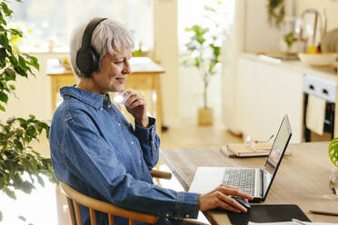 Älterer Freiberufler sitzend mit Hand am Kinn und Laptop im Home Office - EBSF04389