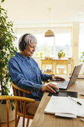Mature freelancer using computer mouse with laptop at home office - EBSF04391