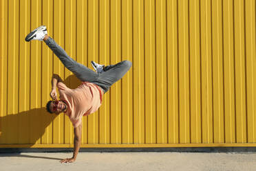 Carefree man doing hand stand in front of yellow striped wall - SYEF00531