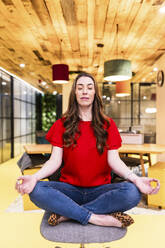 Businesswoman practicing yoga on chair in office - WPEF08452