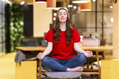 Mature businesswoman meditating on chair in office - WPEF08453