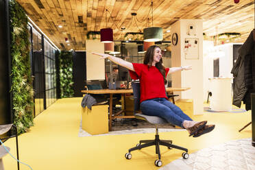 Carefree businesswoman having fun on chair in office - WPEF08456