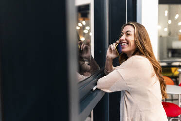 Glückliche Geschäftsfrau, die in der Nähe des Fensters im Büro mit ihrem Smartphone telefoniert - WPEF08467