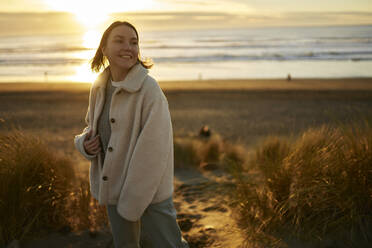Lächelnde junge Frau am Meeresstrand bei Sonnenuntergang - ANNF00858