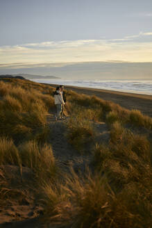 Young couple standing in dune at ocean beach - ANNF00863