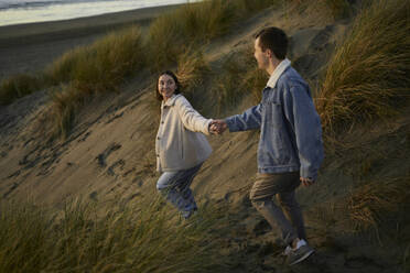 Junge Frau hält die Hand ihres Freundes und geht am Strand spazieren - ANNF00876