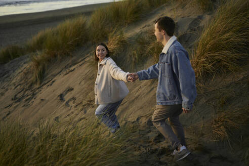Young woman holding hand of boyfriend and walking on beach - ANNF00876