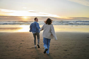 Boyfriend holding hand of girlfriend and running towards sea at beach - ANNF00884
