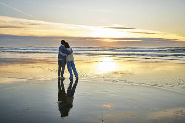 Junge Frau und Mann umarmen sich und genießen den Meerblick am Strand - ANNF00886