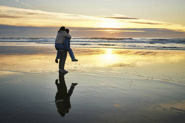 Young man piggybacking girlfriend and walking near sea on beach - ANNF00888