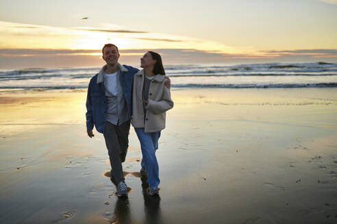 Smiling man walking with girlfriend on ocean beach - ANNF00893