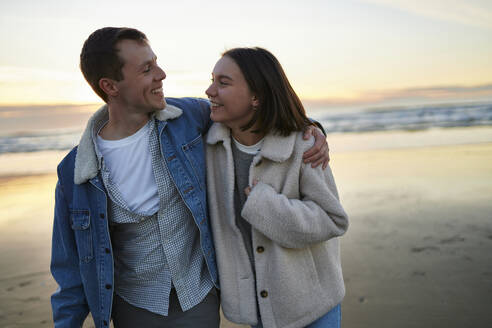 Lächelnder Mann mit Arm um Freundin beim Strandspaziergang - ANNF00894