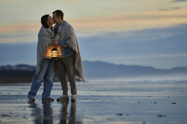 Junger Mann mit Laterne küsst Freundin am Strand - ANNF00900