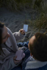 Junges Paar betrachtet einen sich entwickelnden fotografischen Abzug am Strand - ANNF00925