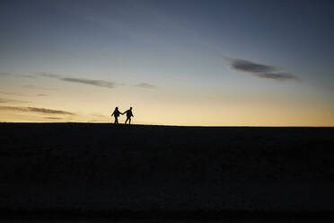 Silhouette of young couple holding hands and walking at beach - ANNF00939