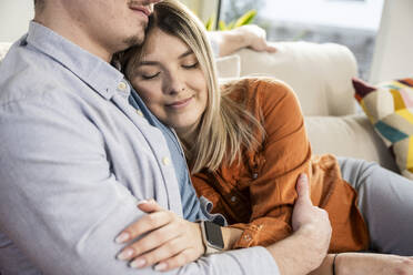 Lächelnde Frau umarmt Mann auf Sofa zu Hause - UUF31341