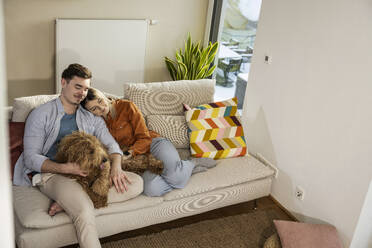 Verliebtes Paar mit Hund auf dem Sofa sitzend - UUF31343