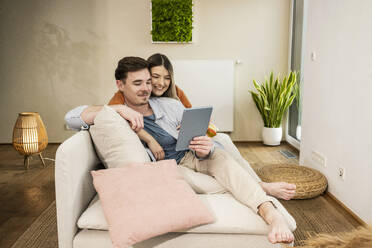 Lächelndes junges Paar mit Tablet-PC auf dem Sofa - UUF31348