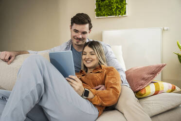 Lächelndes junges Paar bei der Nutzung eines Tablet-PCs im heimischen Wohnzimmer - UUF31350