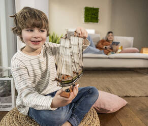 Happy boy sitting with model ship at home - UUF31355