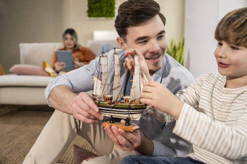 Happy father and son playing with model ship at home - UUF31357