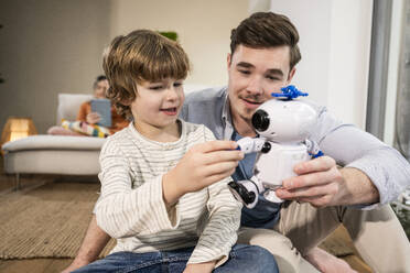 Happy father and son playing with toy robot at home - UUF31358