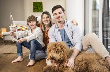 Happy family with model house and dog sitting in living room - UUF31362