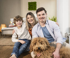 Happy family sitting with dog at home - UUF31364