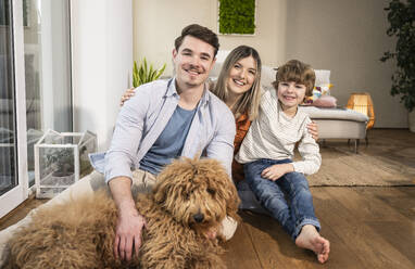 Happy family sitting with dog in living room at home - UUF31365