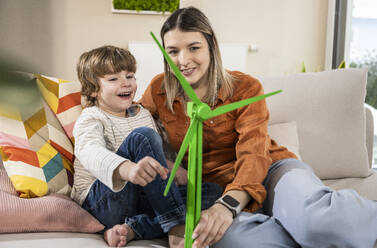 Glückliche Mutter und Sohn mit Windradmodell auf dem Sofa zu Hause - UUF31372