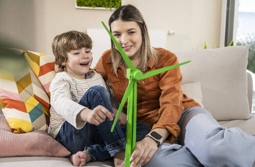 Happy mother and son with wind turbine model on sofa at home - UUF31372