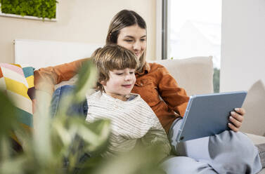 Glückliche Mutter und Sohn benutzen einen Tablet-PC auf dem Sofa zu Hause - UUF31375