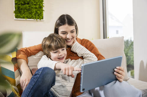 Glückliche Mutter und Sohn benutzen einen Tablet-PC auf dem Sofa im Wohnzimmer zu Hause - UUF31376