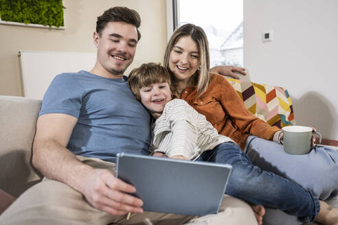 Happy family using tablet PC on sofa at home - UUF31385