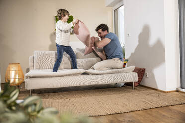 Happy father and son playing pillow fight at home - UUF31386