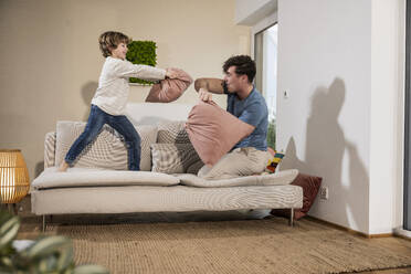Happy father playing pillow fight with son at home - UUF31387