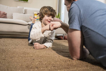 Glücklicher Vater und Sohn beim Faustschlag auf dem Teppich zu Hause - UUF31389