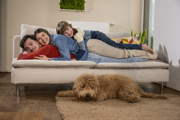 Happy family relaxing on sofa near dog at home - UUF31393