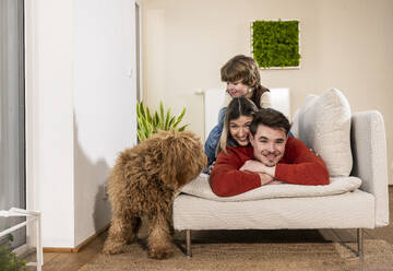 Glückliche Familie auf dem Sofa liegend in der Nähe von Hund zu Hause - UUF31395