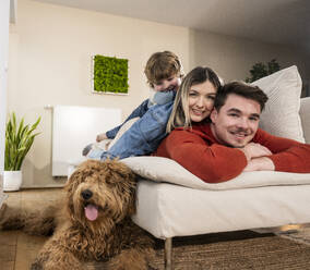 Smiling family lying on sofa near dog at home - UUF31396