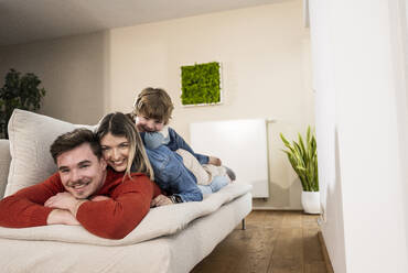 Happy family lying together on sofa at home - UUF31398