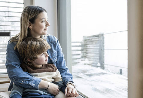 Lächelnde Mutter und Sohn schauen durch das Fenster zu Hause - UUF31400